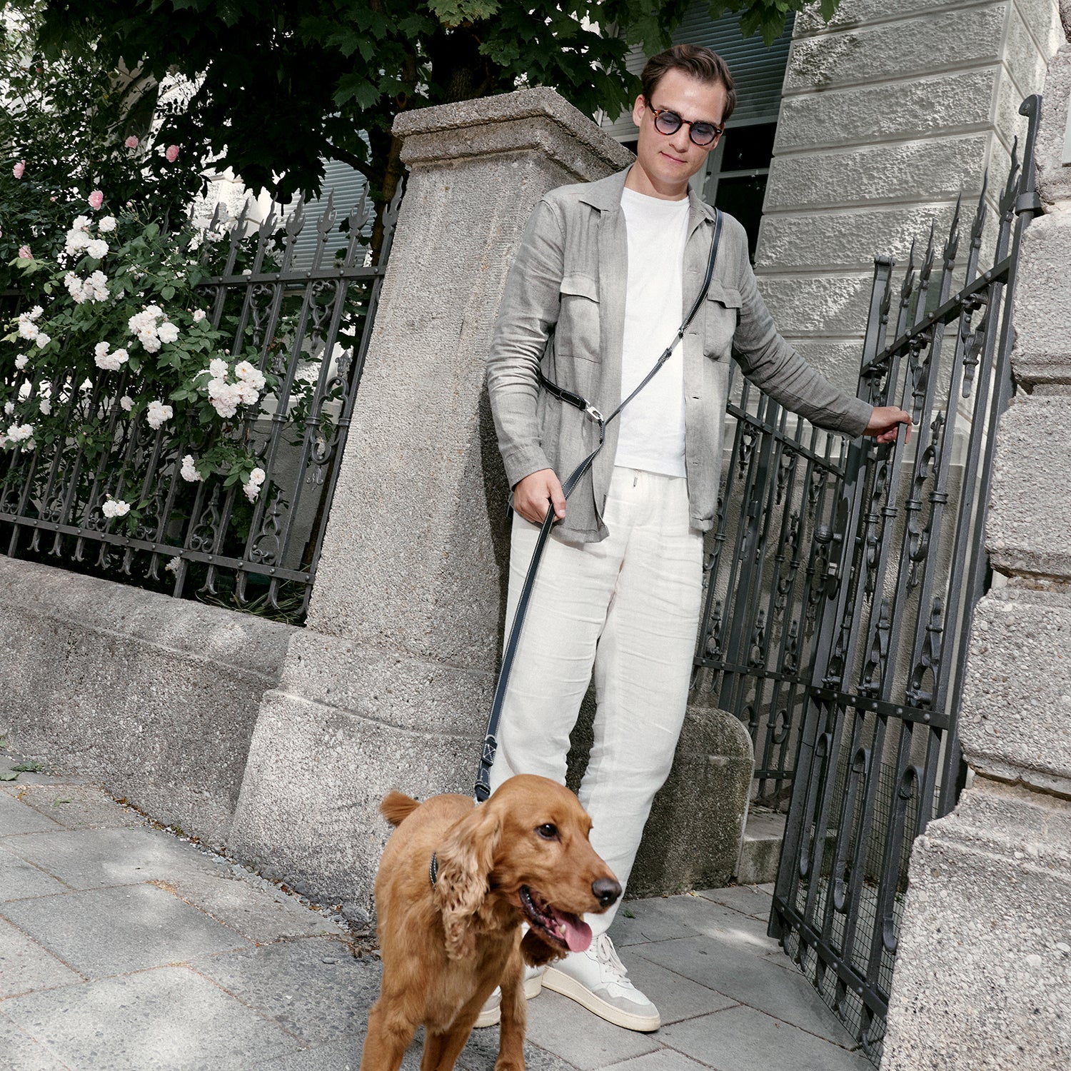 Uomo in abiti di lino accanto a un cancello in ferro battuto con il suo Cocker Spaniel al Guinzaglio Bond Studio Camour color Black, indossato a tracolla